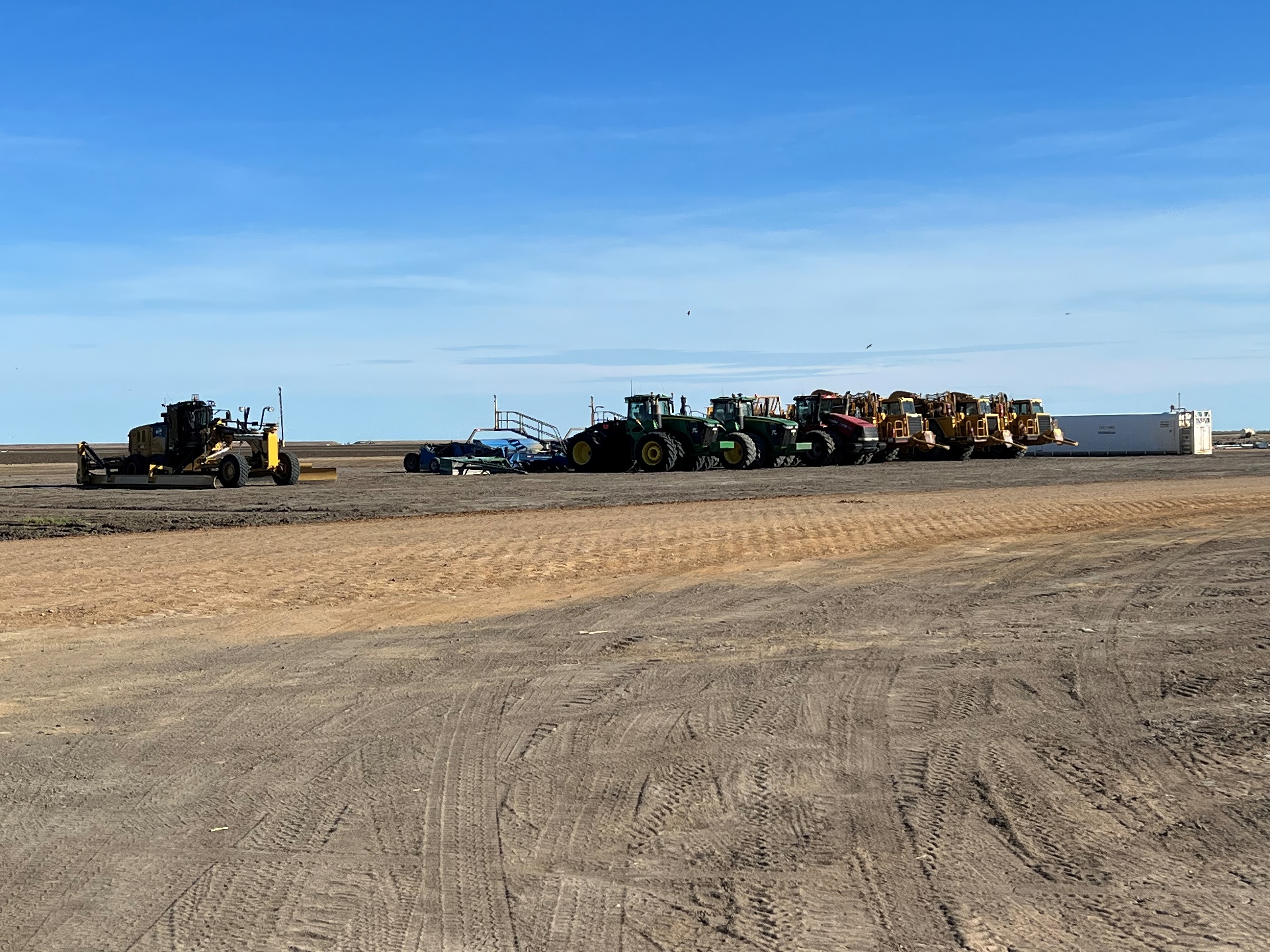 A number of tractors and large machinery are lined up in a dirt paddock